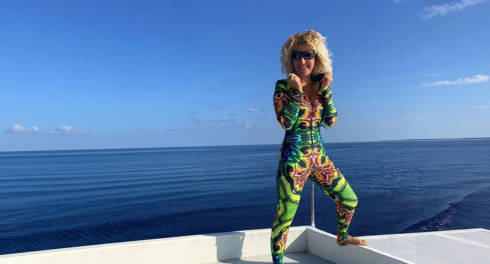 Person wearing a colorful patterned outfit standing on a boat with ocean and sky in the background
