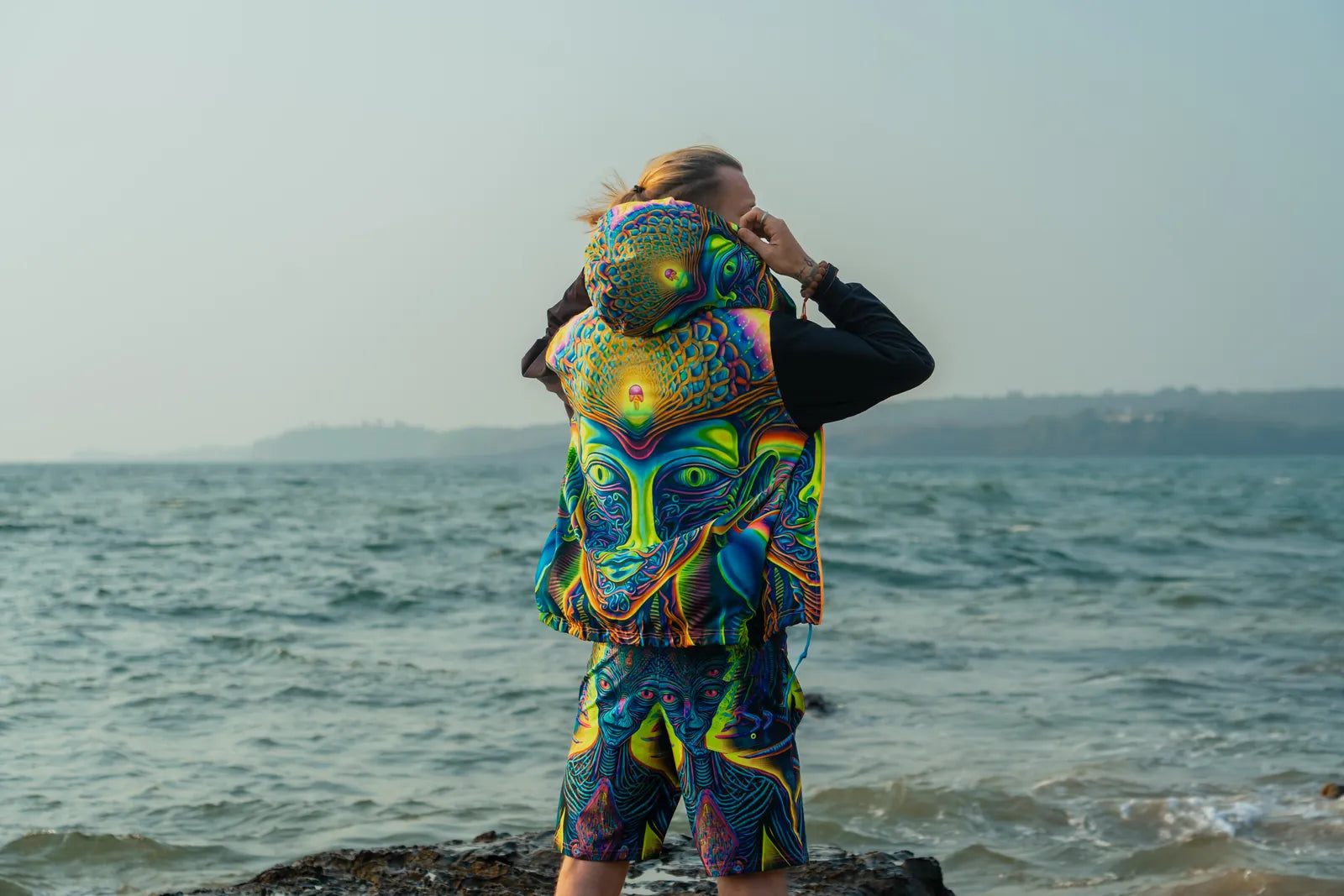 Person with a colorful psychedelic-patterned backpack standing on a beach.
